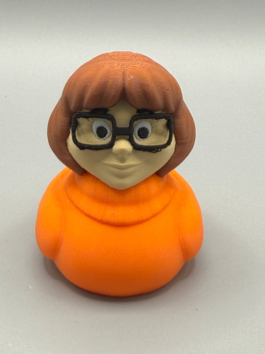 Velma Duck – front view showing oversized black glasses, round eyes, and bright orange body